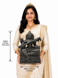 Hand-carved 1.25 ft Saraswathi Devi statue in polished black stone shown beside an adult model for scale.